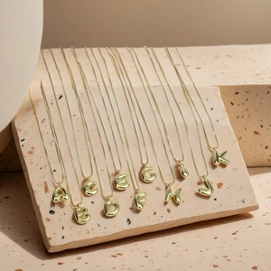Polished gold initial letter pendant necklaces displayed on a beige stone surface