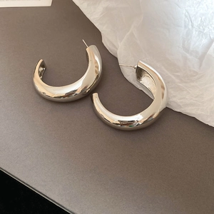 Detailed view of chunky silver-toned twisted C-shape hoop earrings on dark background