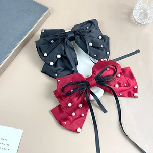 Detail view of large red and black satin bow hair clips with pearls and long tassels