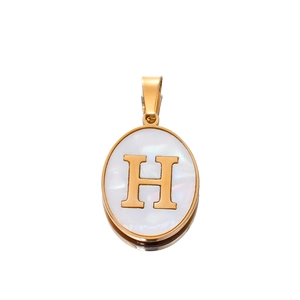 Macro detail of oval gold pendant with white shell inlay and gold letter H charm