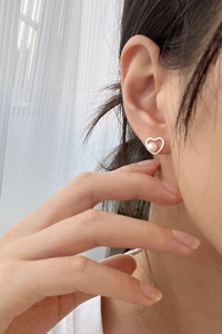 Close-up of minimalist silver heart stud earring with inlaid freshwater pearl on model