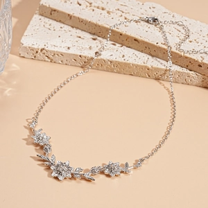 Détail macro du collier fleurs et feuilles argenté sur pierre texturée avec finition métal