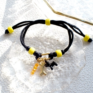 Detail of black braided DIY bracelet with yellow beads and golden dog bone charms