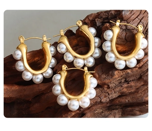 Close-up of U-shaped gold plated earrings with white pearls on a textured wood background