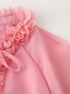 Detail of pink chiffon top featuring tiered ruffle neckline and delicate bow tie closure