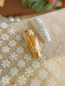 Macro shot of 3D embossed white snowflake nail stickers on gold and silver glitter nails