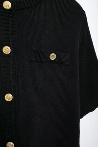 Close-up of black knit fabric texture and ornate golden embossed buttons on a dress