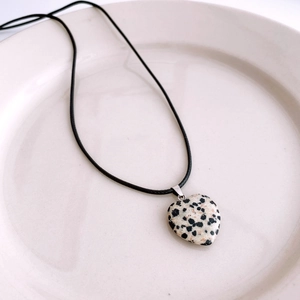 Vue détaillée d'un pendentif cœur en pierre tachetée avec cordon noir sur une assiette