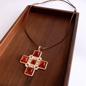 Close-up of amber cross pendant with pearls on a brown cord over a wooden texture