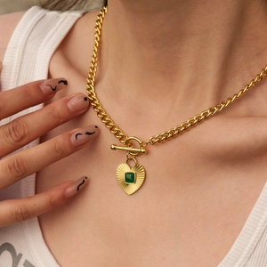 Detailed close-up of golden chunky chain necklace with emerald stone heart pendant and T-bar clasp