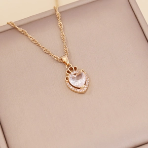 Close-up of gold crown heart pendant with large clear gemstone on beige jewelry pad