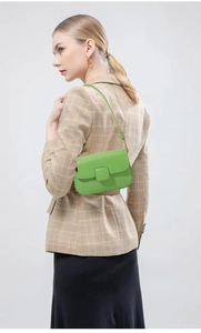 Detail of green leather shoulder bag with chic square buckle worn by a model