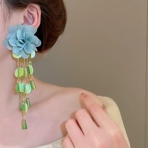 Detailed view of long fabric flower earrings with green sequin tassels on model