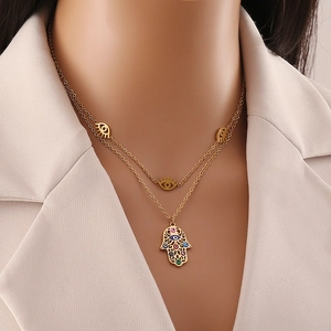 Detailed view of gold multi-layer necklace with Hamsa hand and evil eye charms on model
