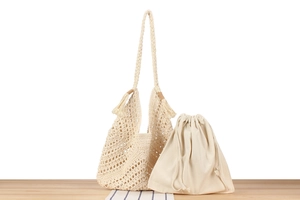 Detail of a beige handmade crochet shoulder bag with hollow mesh pattern and drawstring pouch