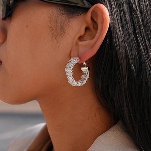 Boucles d'oreilles créoles argentées texturées portées par un mannequin en vue latérale