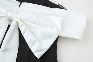 Detail of a large white satin bow on a black asymmetric dress with smooth fabric texture