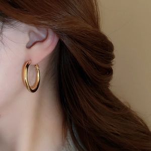 Close-up of chunky gold hoop earrings with a polished metallic finish on a model