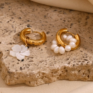 Detailed view of asymmetrical gold-plated flower and pearl earrings on stone texture