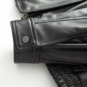 Detailed view of the cuffs with metal snap buttons and elastic hem on black faux leather jacket