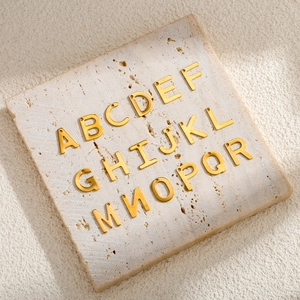 Golden stainless steel letter charms A to R arranged on a textured stone plate