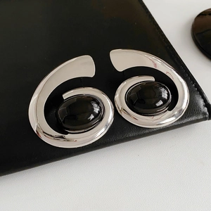 Detail of silver spiral earrings featuring an oval black gemstone on black leather