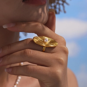 Golden wavy textured open ring with white pearl accent shown in stylish outdoor setting