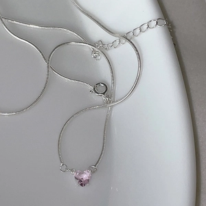 Close-up of a silver-toned necklace featuring a pink heart zircon pendant on white porcelain