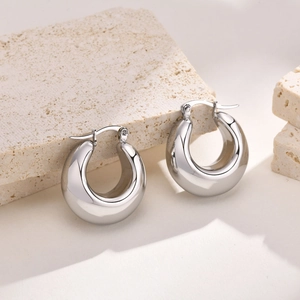 Macro shot of silver hollow thick hoop earrings on stone with high-polish texture