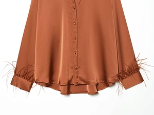 Detail of satin shirt sleeve with elegant feather trim and covered buttons in caramel