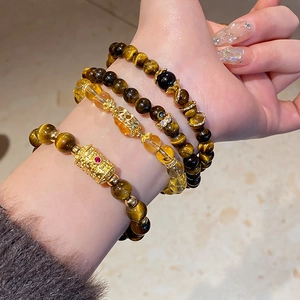 Detail view of stacked tiger eye and citrine beaded bracelets with gold floral charms