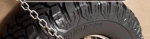 Close-up of off-road tire with deep grooves and metal snow chains for winter safety