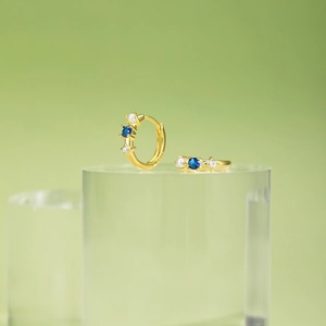 Detailed close-up of S925 silver gold earring with blue zircon and a small white pearl