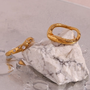 Detail of 18K gold plated wavy rings with crystal inlay on wet marble stone background