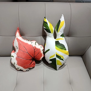Set of two creative leaf-shaped plush pillows in tropical foliage patterns on a sofa