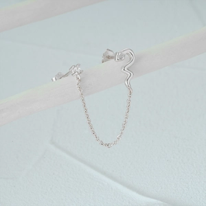 Close-up of a s925 silver snake chain earring with white zircon stone on a white branch