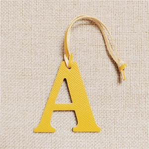 Detailed view of yellow leather letter A bag charm on beige textured fabric background