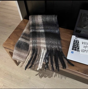 Detail of a thick plaid scarf with tassels on a wooden chair in a cozy setting