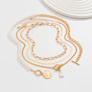Detail of baroque pearl necklace set with layered gold chains and coin pendant on white