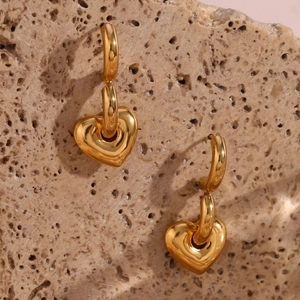 Close-up of gold heart pendant hoop earrings displayed on a textured stone surface