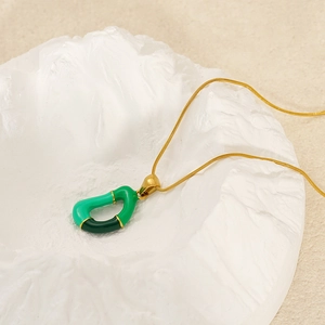 Collana con ciondolo a lettera dorata e smalto verde su uno sfondo strutturato