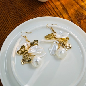 Close-up of golden butterfly petal pearl earrings with delicate tassel details