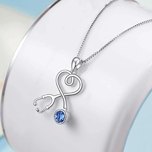 Close-up of heart-shaped stethoscope necklace with a blue gemstone on a white stand