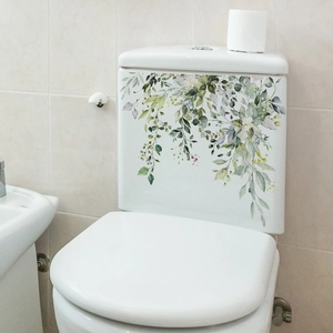 Close-up of watercolor green leaf stickers on a white toilet tank in a bathroom setting