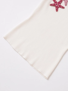 Macro detail of pink sequin starfish embroidery on white knitted sleeveless top