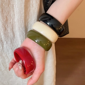 Gros plan de quatre bracelets en résine acrylique noire, crème, olive et rouge sur un poignet