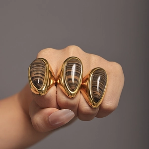 Hand wearing three 18K gold teardrop wood grain stone rings against a gray wall background