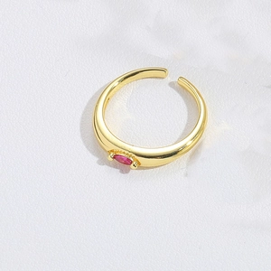 Close-up of golden open ring featuring a delicate red gemstone inlay on white background