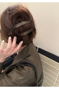 Détail d'une pince à cheveux ovale marron foncé avec paillettes dorées sur les cheveux d'une femme