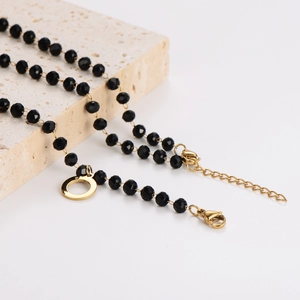 Minimalist black faceted glass bead necklace with a gold round pendant on beige stone